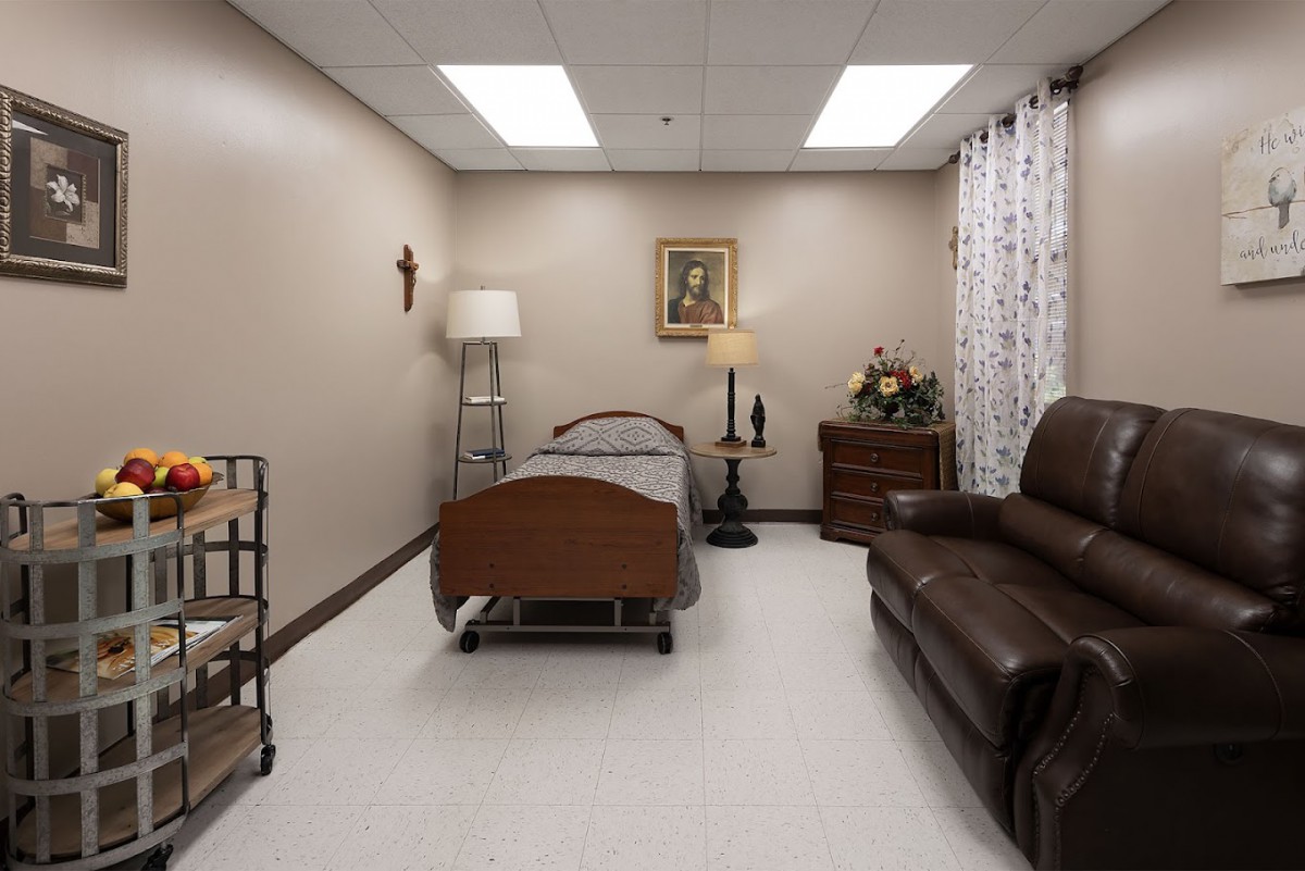 A hospital room featuring a bed, couch, lamp, and decorative elements.