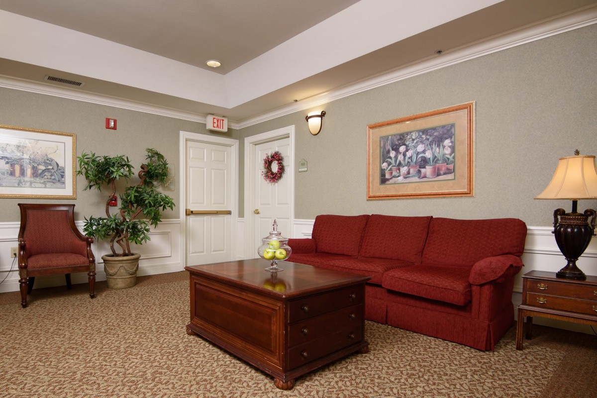 A cozy living room with a red sofa, wooden coffee table, potted plant, and decorative artwork.
