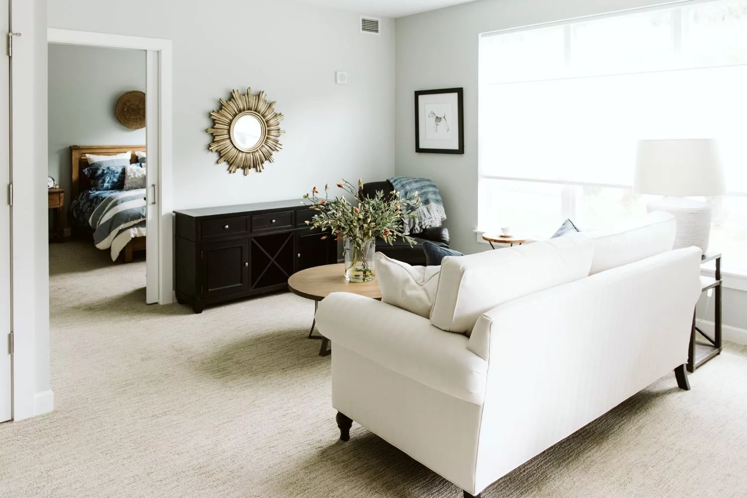A bright and minimalist living room featuring a white sofa, wooden coffee table, and decorative mirror.