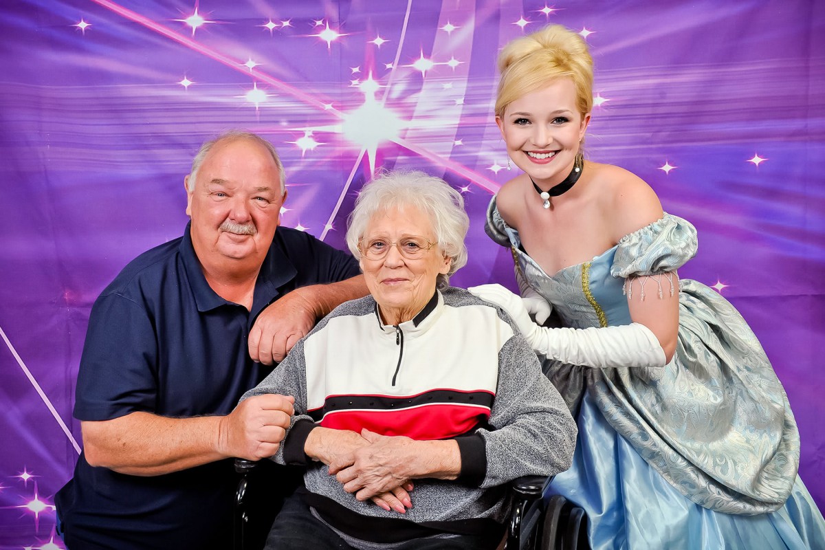 A joyful moment with a costumed character posing alongside an elderly person in a wheelchair and another smiling individual.