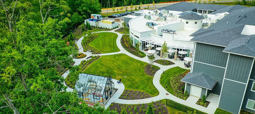 An aerial view of a modern building surrounded by landscaped gardens and pathways, featuring a small greenhouse.