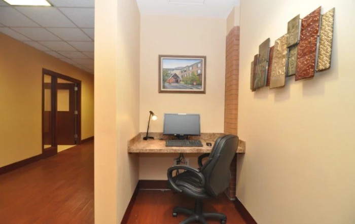 A small office nook with a desk setup, including a computer and lamp, complemented by wall art.