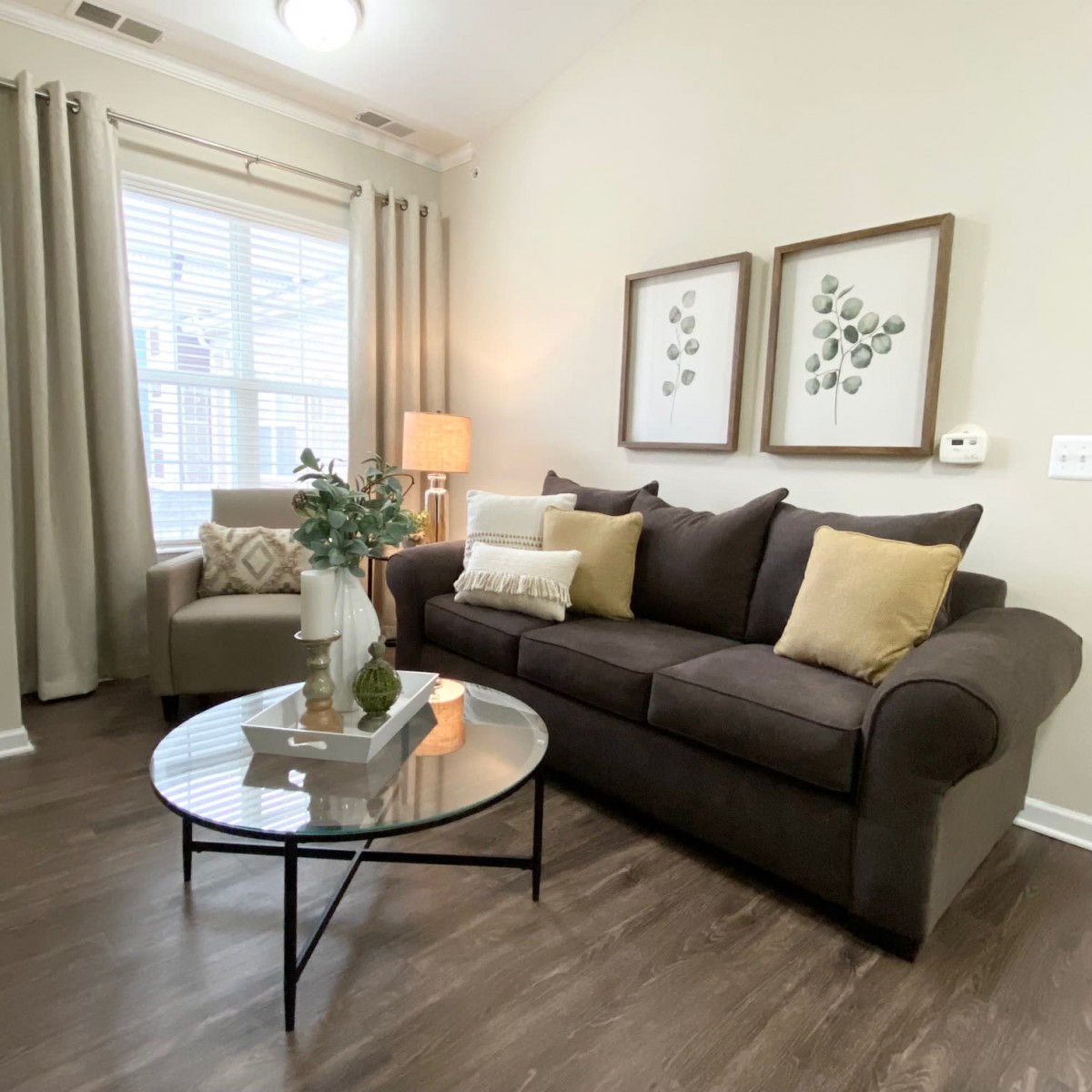 A cozy living room with a dark sofa, decorative pillows, and a round glass coffee table.
