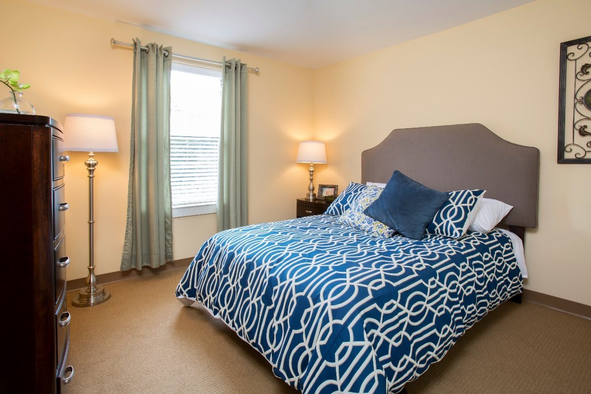 A cozy bedroom featuring a bed with blue patterned bedding, two lamps, and a window with light curtains.