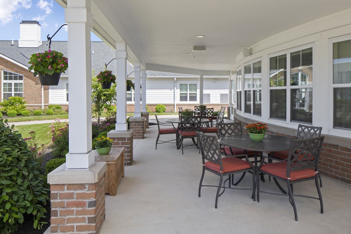 A spacious outdoor patio with tables and chairs under a covered area, featuring hanging plants and brick accents.
