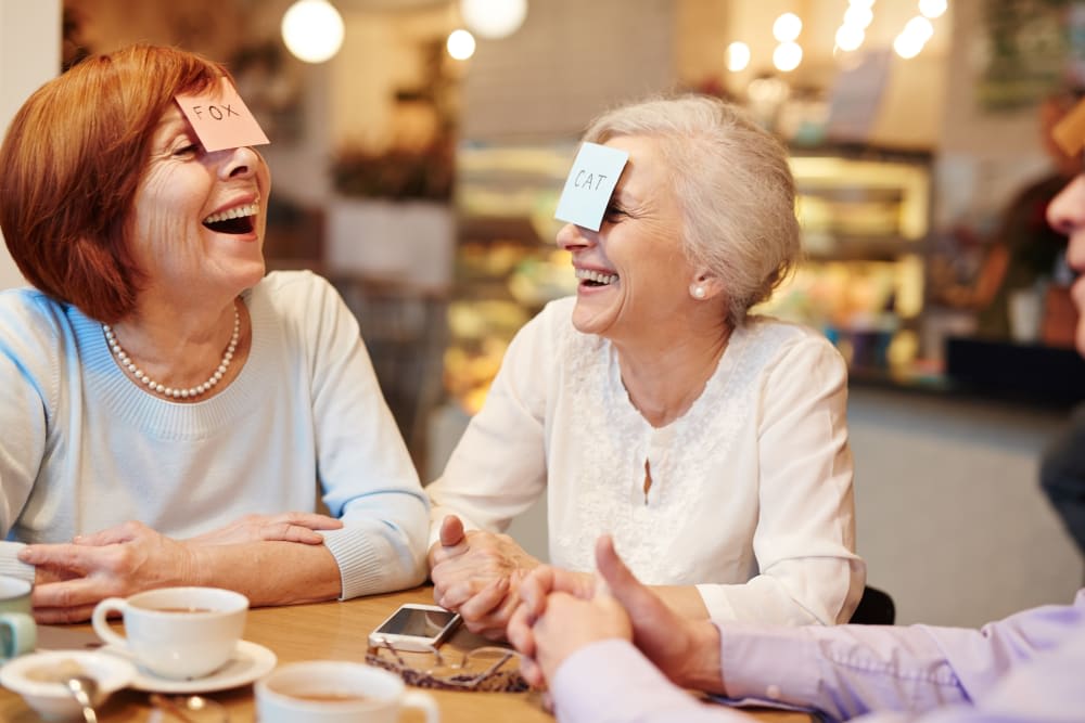 A group of seniors laughing and enjoying a game with post-it notes on their foreheads at a cafe.