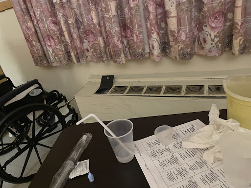 A snapshot of a room featuring a table with a plastic cup, straw, and cleaning materials, alongside floral curtains.