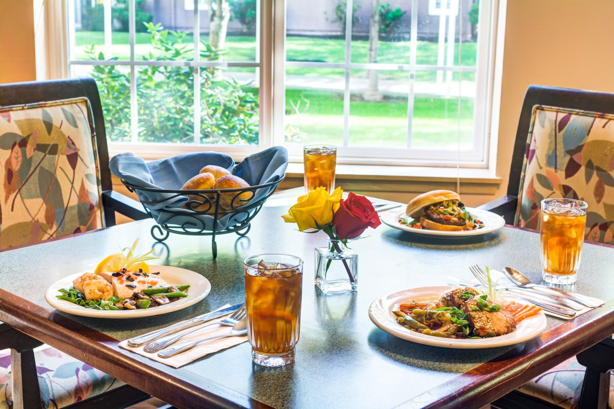 A beautifully set dining table with delicious meals and refreshing drinks near a sunny window.
