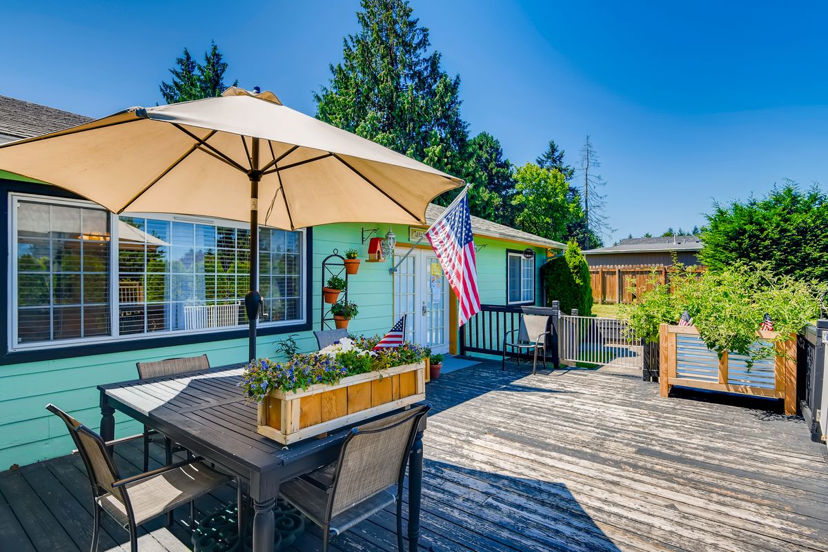 A sunny deck with outdoor furniture and an umbrella, featuring a garden and an American flag.