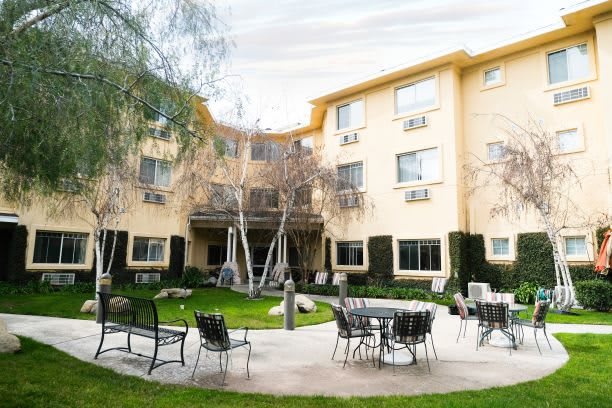 A view of a building with a courtyard featuring tables, chairs, and surrounding greenery.