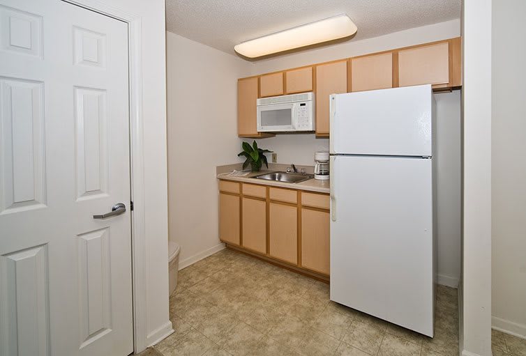 Small minimalist kitchen with light wood cabinets and white appliances.