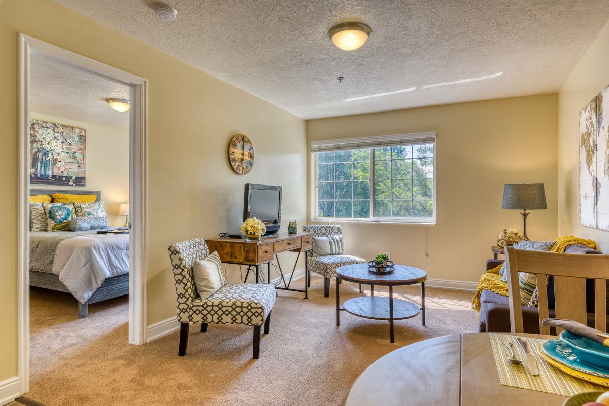 A cozy living room with modern decor, featuring comfortable chairs, a small table, and a large window providing natural light.