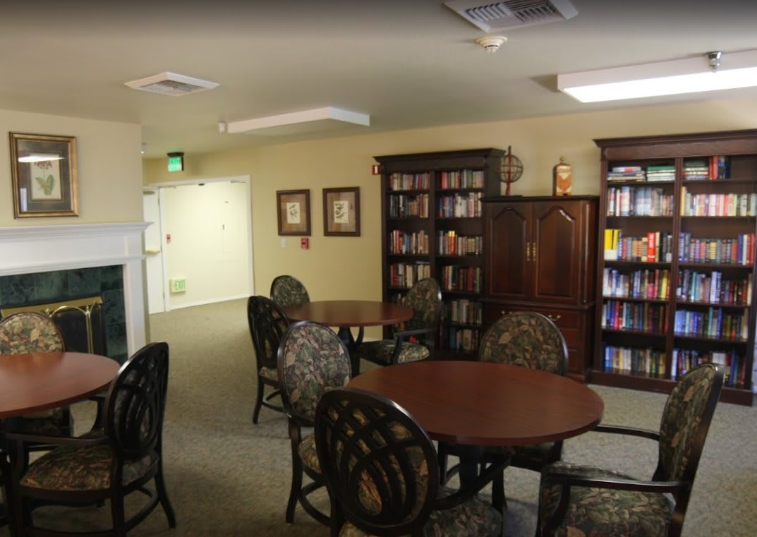 A quiet library room with round tables, chairs, and bookshelves filled with books.