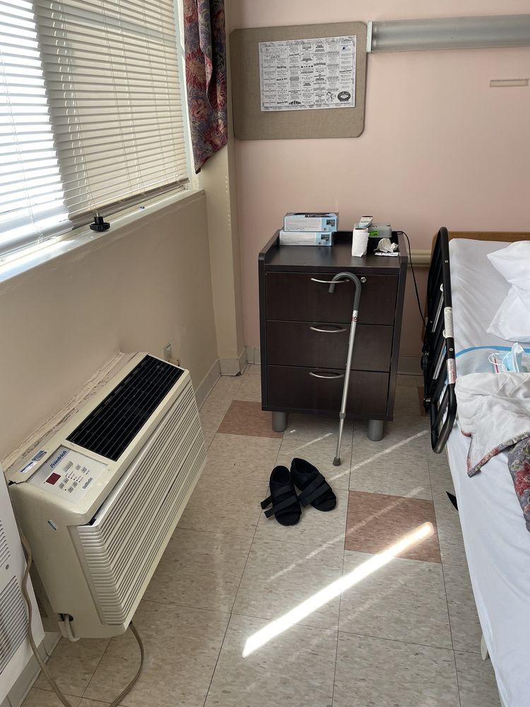 A hospital room with medical equipment, including a walker and an air conditioning unit.