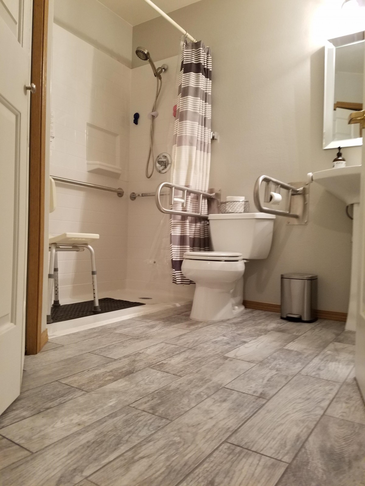 A modern, accessible bathroom featuring a shower with grab bars, toilet, and sink.