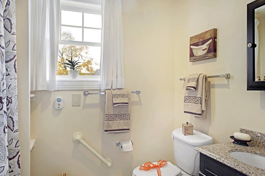 A cozy bathroom featuring beige walls, neatly hung towels, decorative items, and a window letting in natural light.
