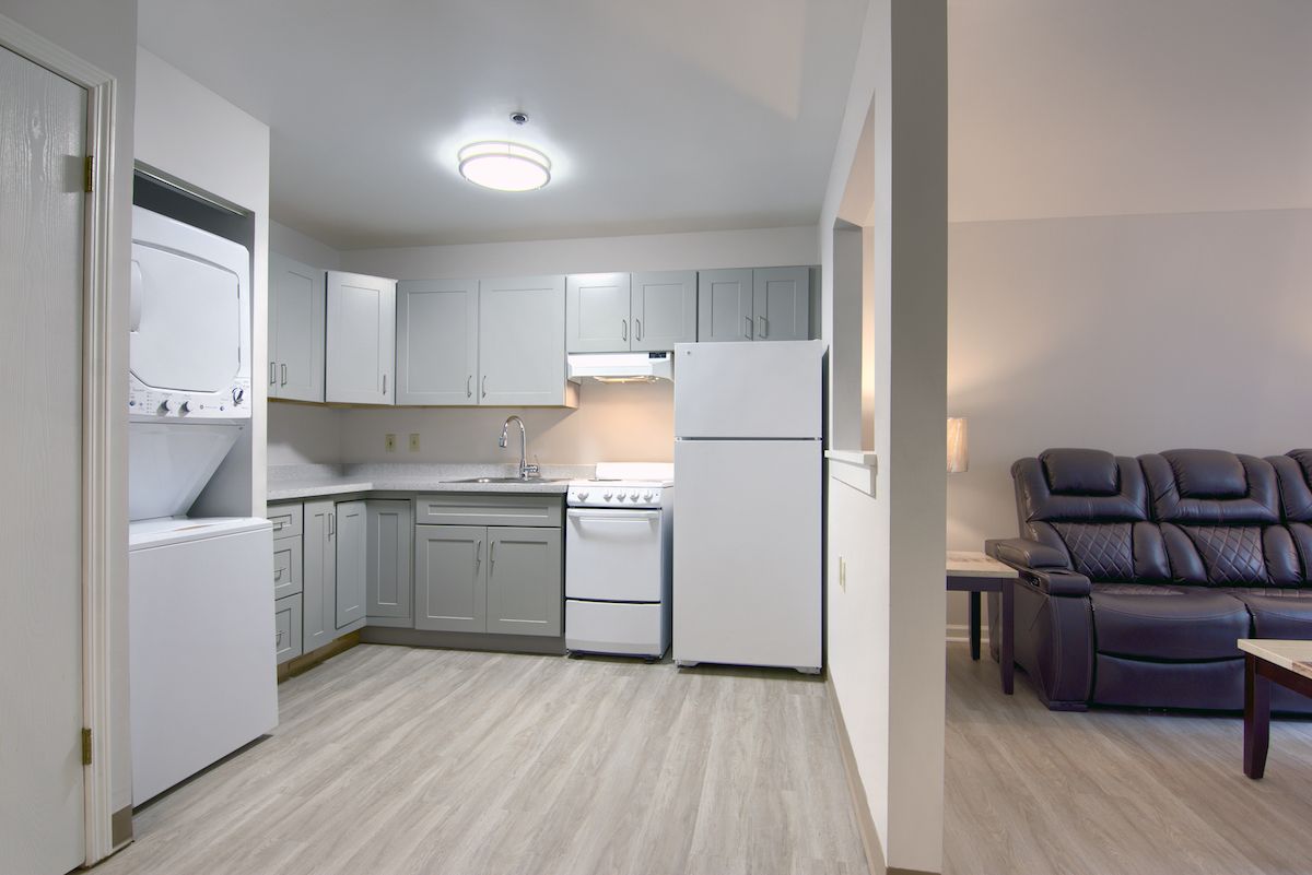 Modern apartment kitchen with light wood flooring and white cabinetry.
