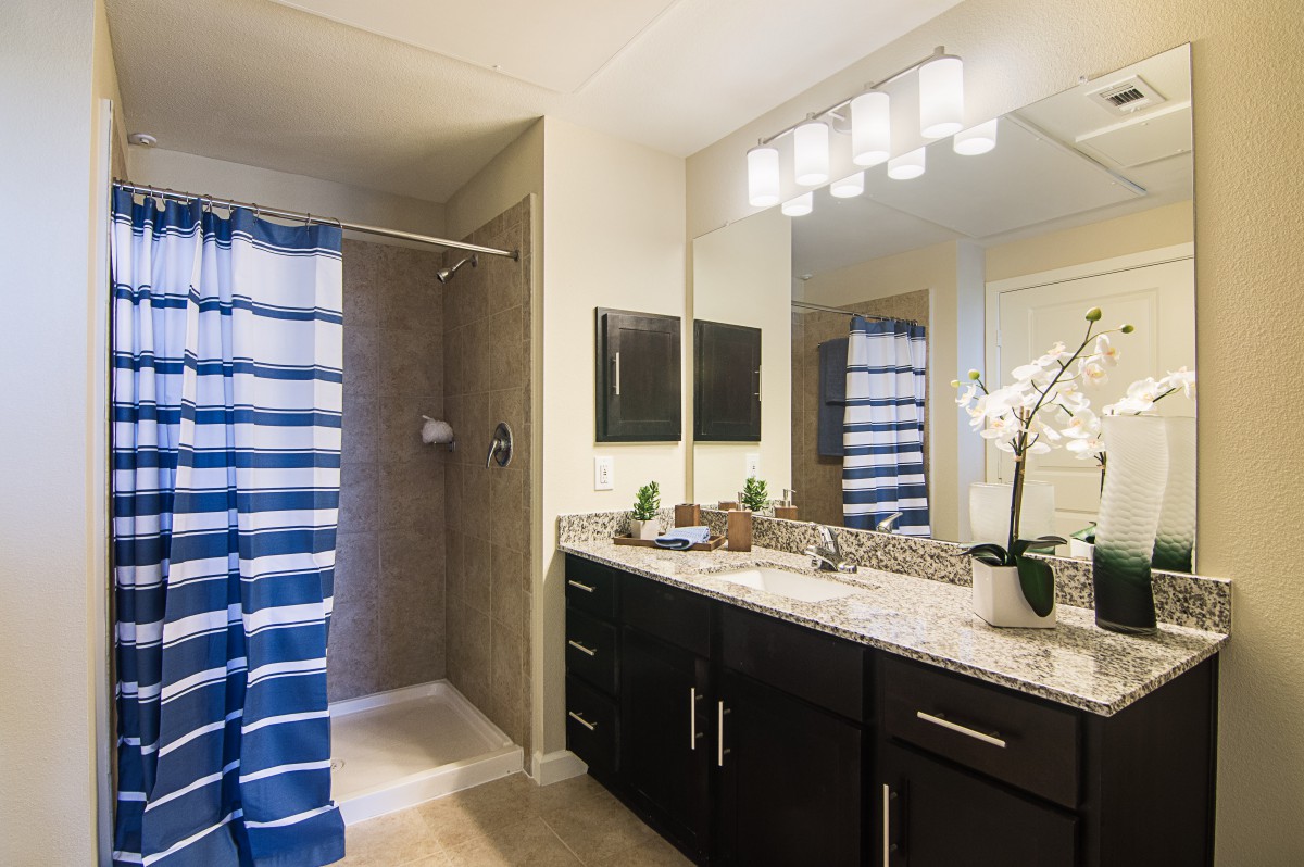 A modern bathroom with a striped blue shower curtain, double sink vanity, and elegant lighting.