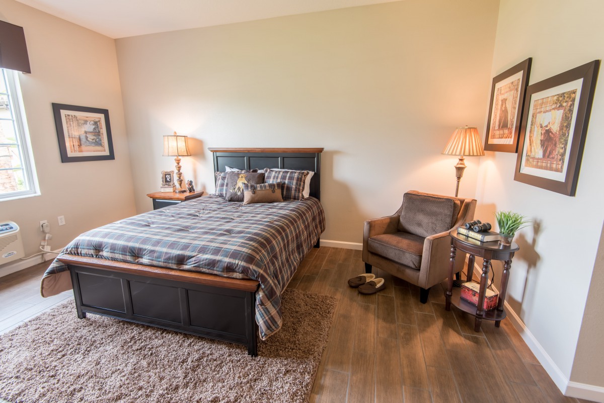 A cozy bedroom with a bed, chair, and soft lighting.