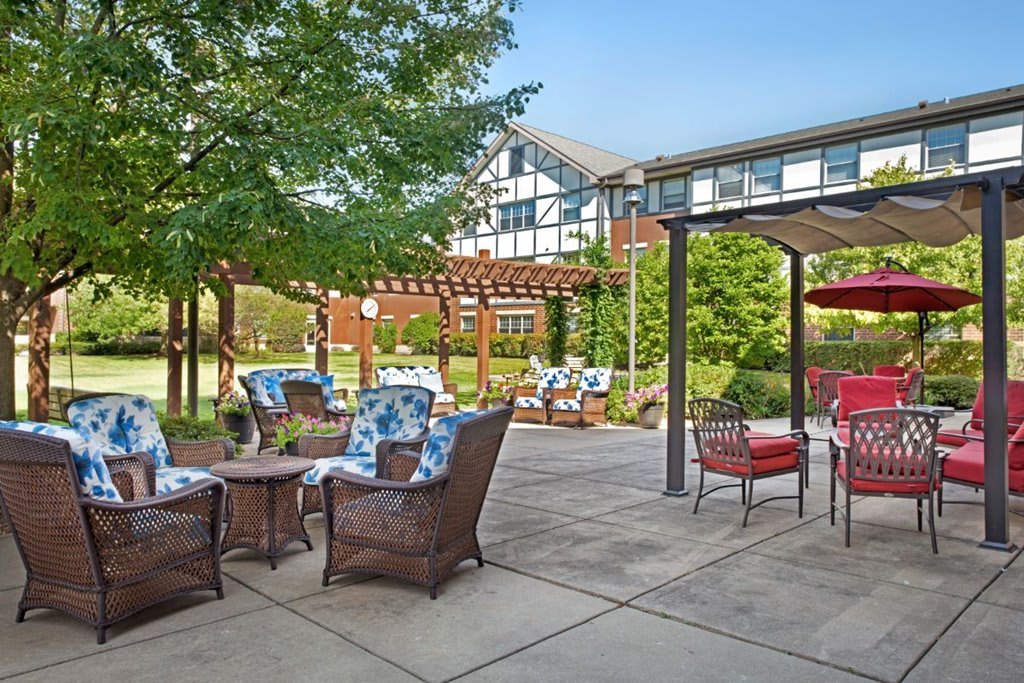 A cozy outdoor patio with comfortable furniture and a pergola surrounded by lush greenery.