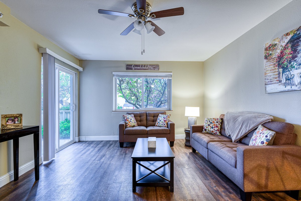 A cozy living room with a wooden floor, featuring two sofas, a coffee table, and a ceiling fan.