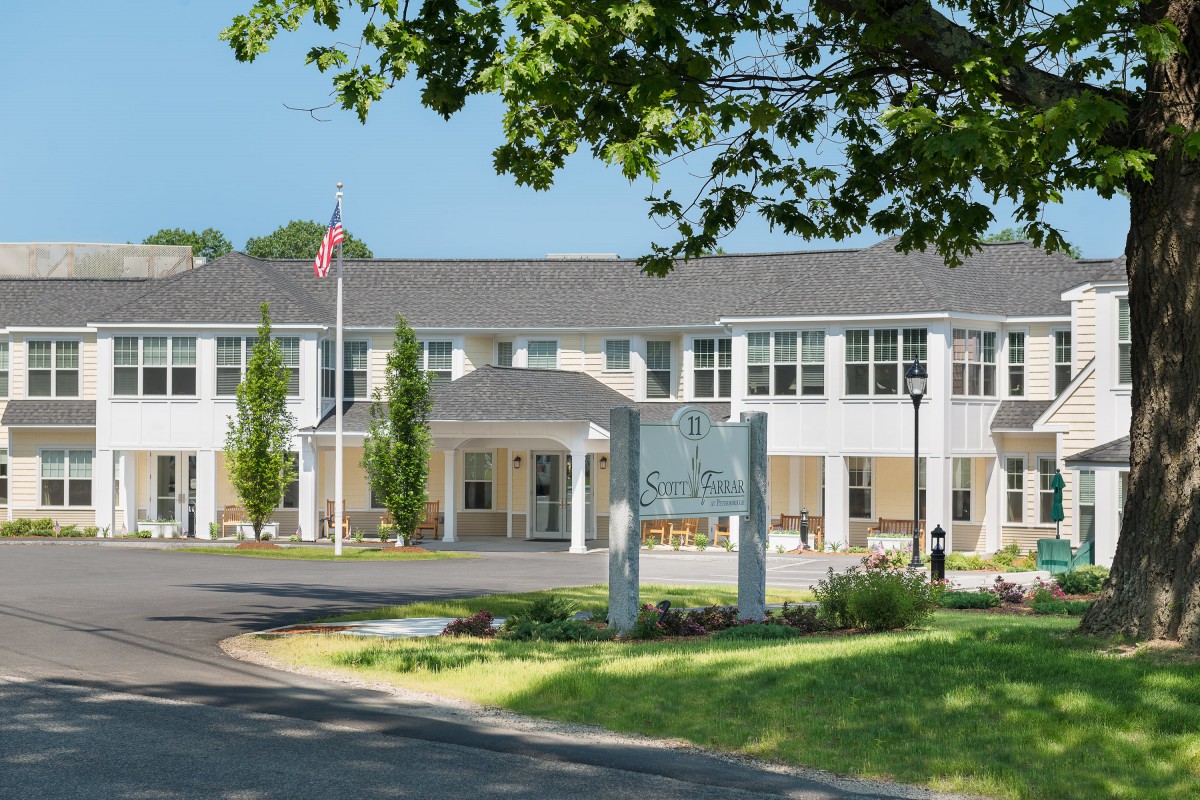 A hospital building with an American flag, surrounded by trees and a sunny sky.