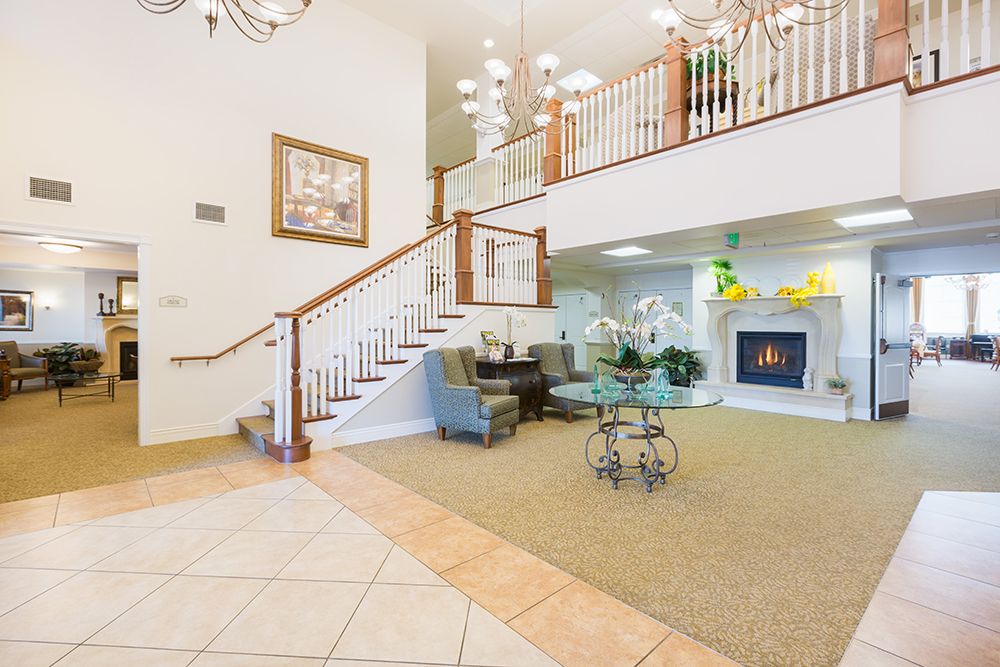 A spacious living room featuring a grand staircase, elegant chandelier, and cozy seating area by the fireplace.