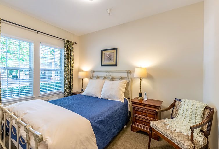 A cozy bedroom with a bed, nightstands with lamps, a window with curtains, and a decorative painting on the wall.