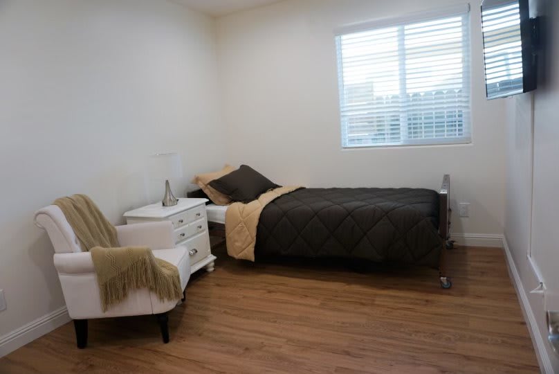 A minimalist bedroom with a single bed, nightstand, and chair on wooden flooring.