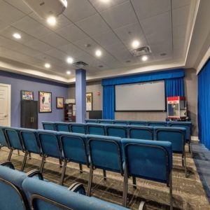 A small theater with rows of blue seating facing a large screen.