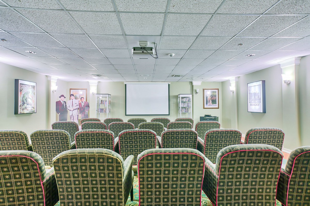 A small conference room with rows of patterned chairs facing a projector screen.