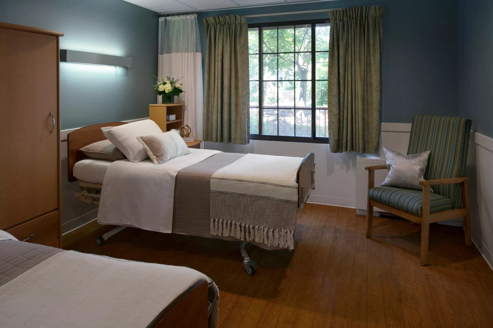 A well-lit hospital room with twin beds and a large window.
