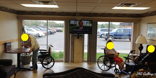 A serene waiting area with two individuals in wheelchairs, watching a news broadcast on the television.