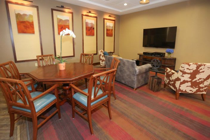 A cozy living room with a dining area, featuring a wooden table and chairs, a sofa, and a television.