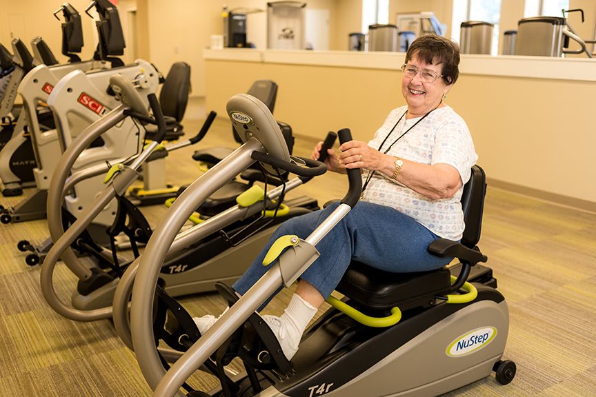 A senior woman enjoying a workout on a cardio machine in the gym while wearing headphones.
