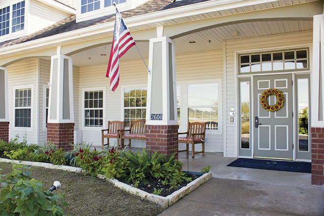 Front porch of a house with an American flag and patio chairs.