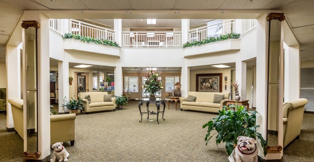 A spacious and elegantly decorated lobby area with sofas, plants, and a central table.