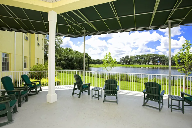 A covered patio with chairs overlooking a tranquil lake and greenery.