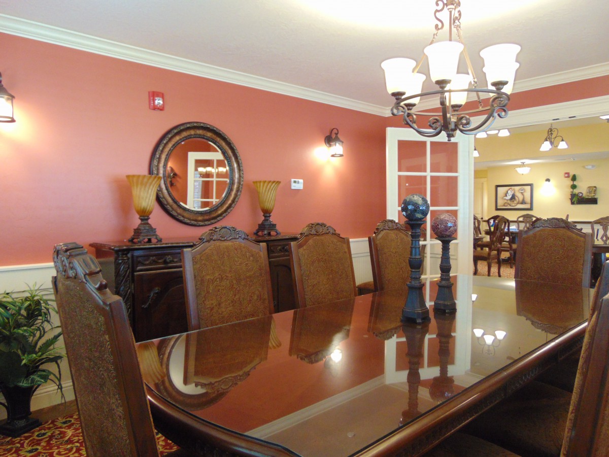 A stylish dining room with a large wooden table and ornate chairs, illuminated by an elegant chandelier.