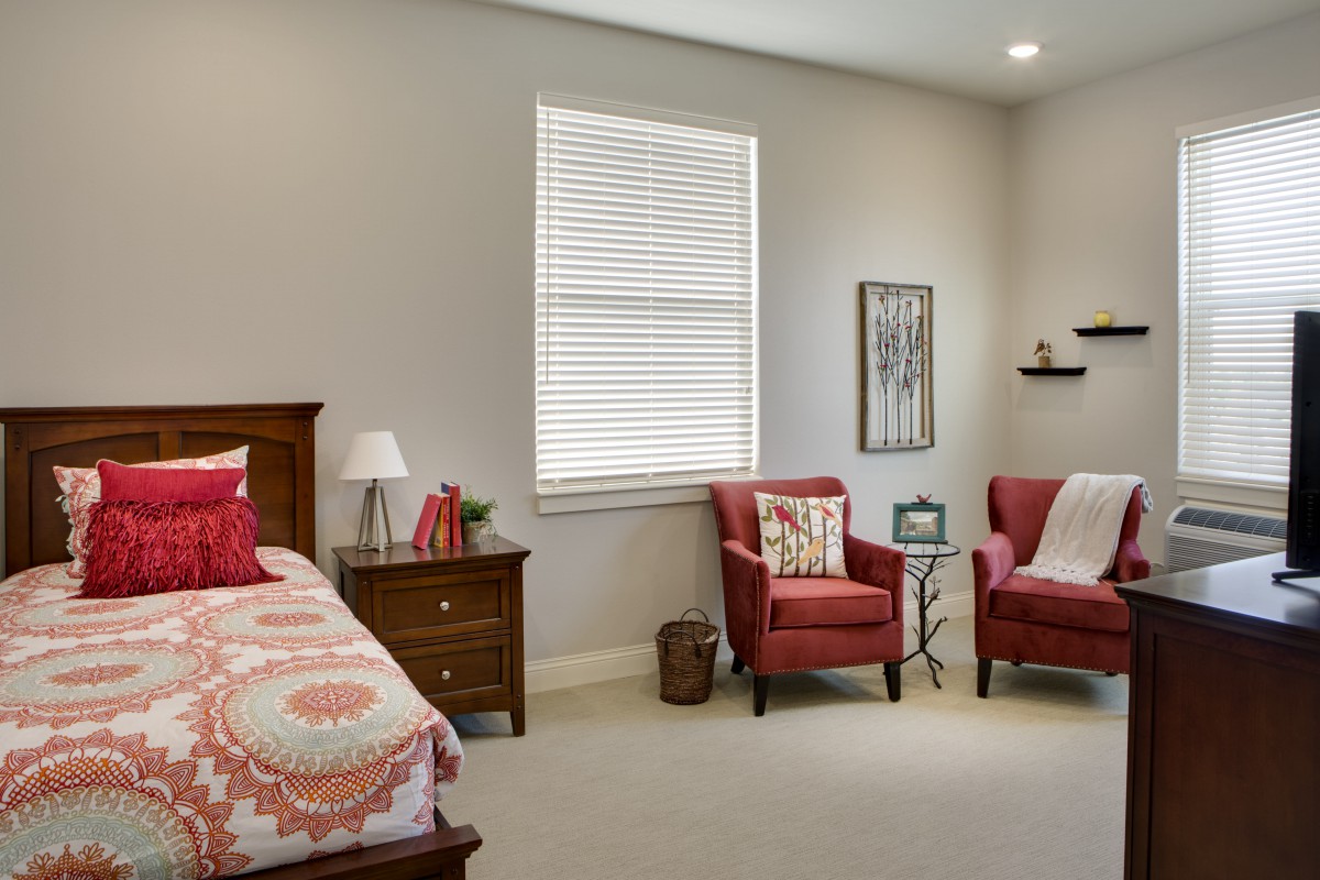 A cozy bedroom with red chairs and a neatly made bed.