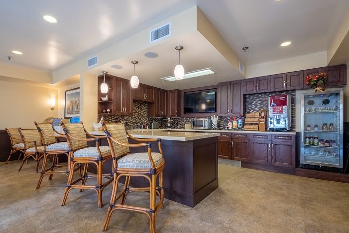 A modern kitchen with wooden cabinets and an island countertop, accompanied by bar stools and pendant lighting.