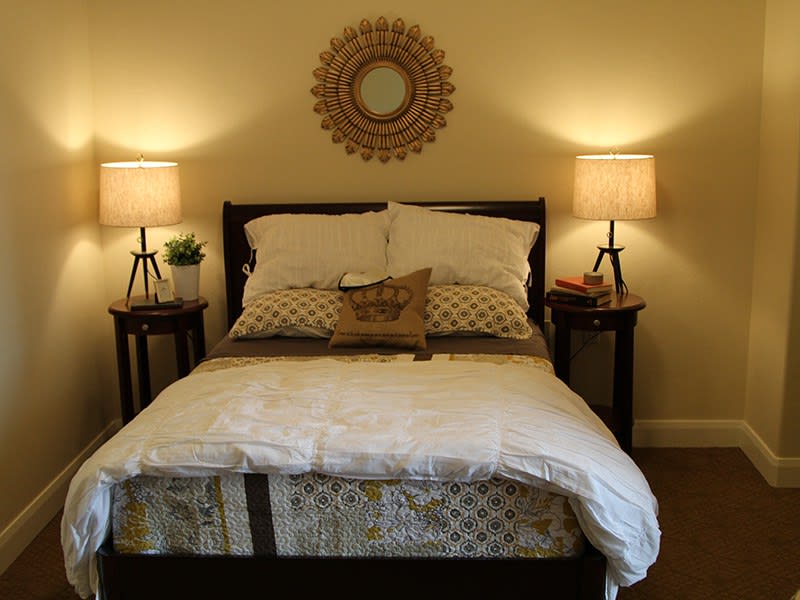 A cozy bedroom with a neatly made bed, flanked by nightstands and warmly lit lamps.