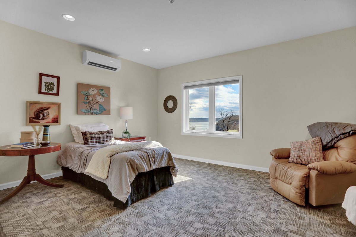 A cozy bedroom with a neatly made bed, art on the walls, and a comfortable armchair by the window.