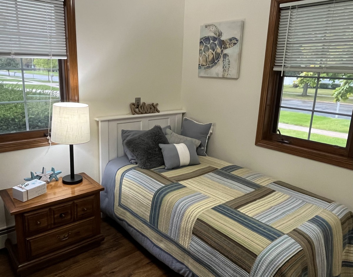 A cozy bedroom with a neatly made bed, bedside table, and warm lighting.
