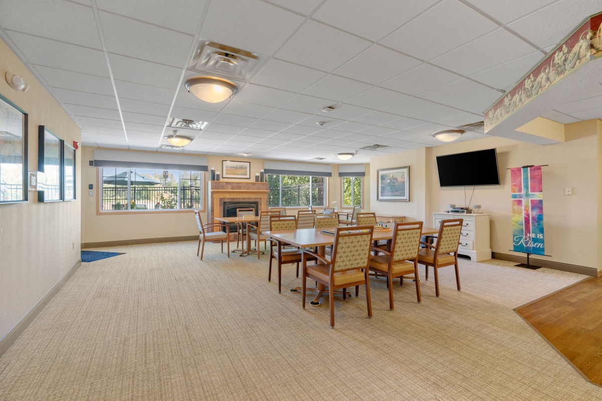 A spacious and well-lit dining area with tables, chairs, a television, and large windows.