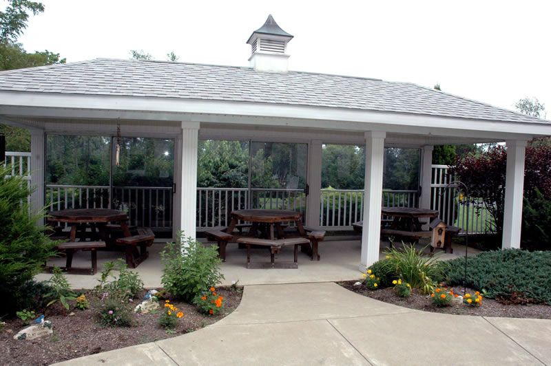 An outdoor gazebo surrounded by a garden with several picnic tables inside.