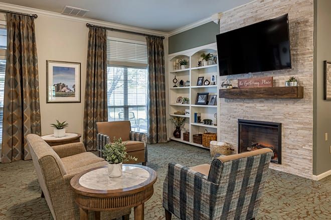 A cozy living room with comfortable armchairs, a fireplace, and a television mounted above bookshelves.