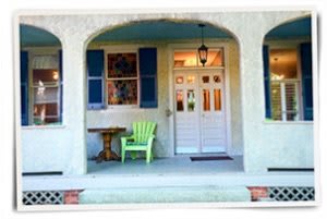 A cozy porch with a green chair and table in front of a double doorway.