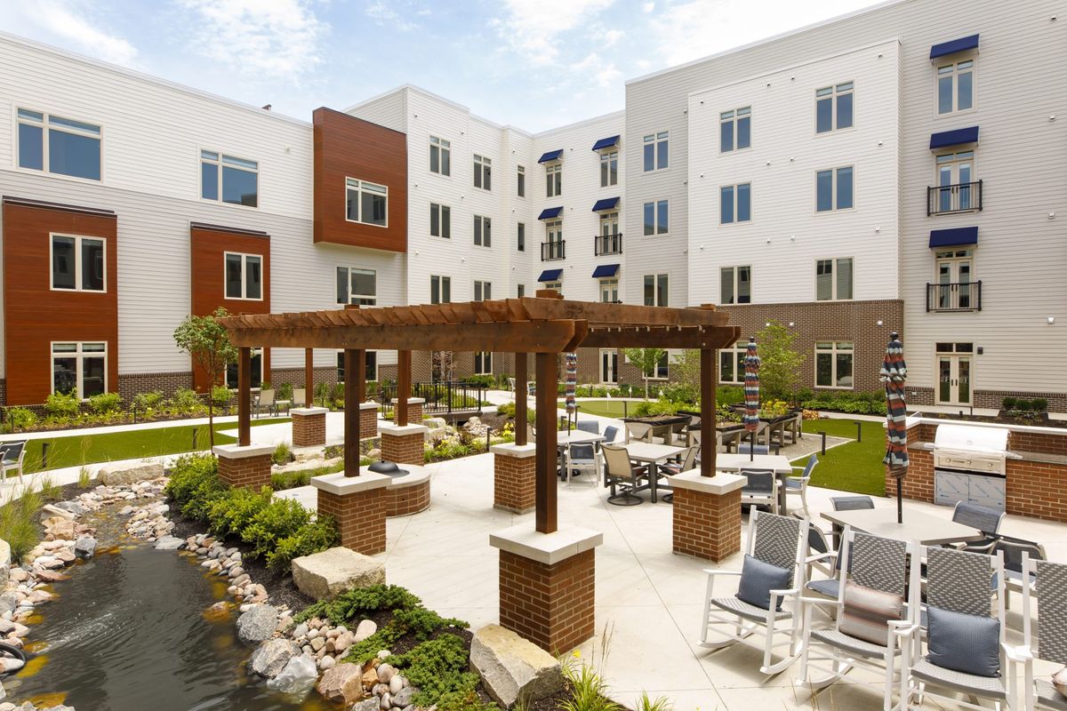 A modern apartment complex with a landscaped courtyard featuring a pergola and outdoor seating.