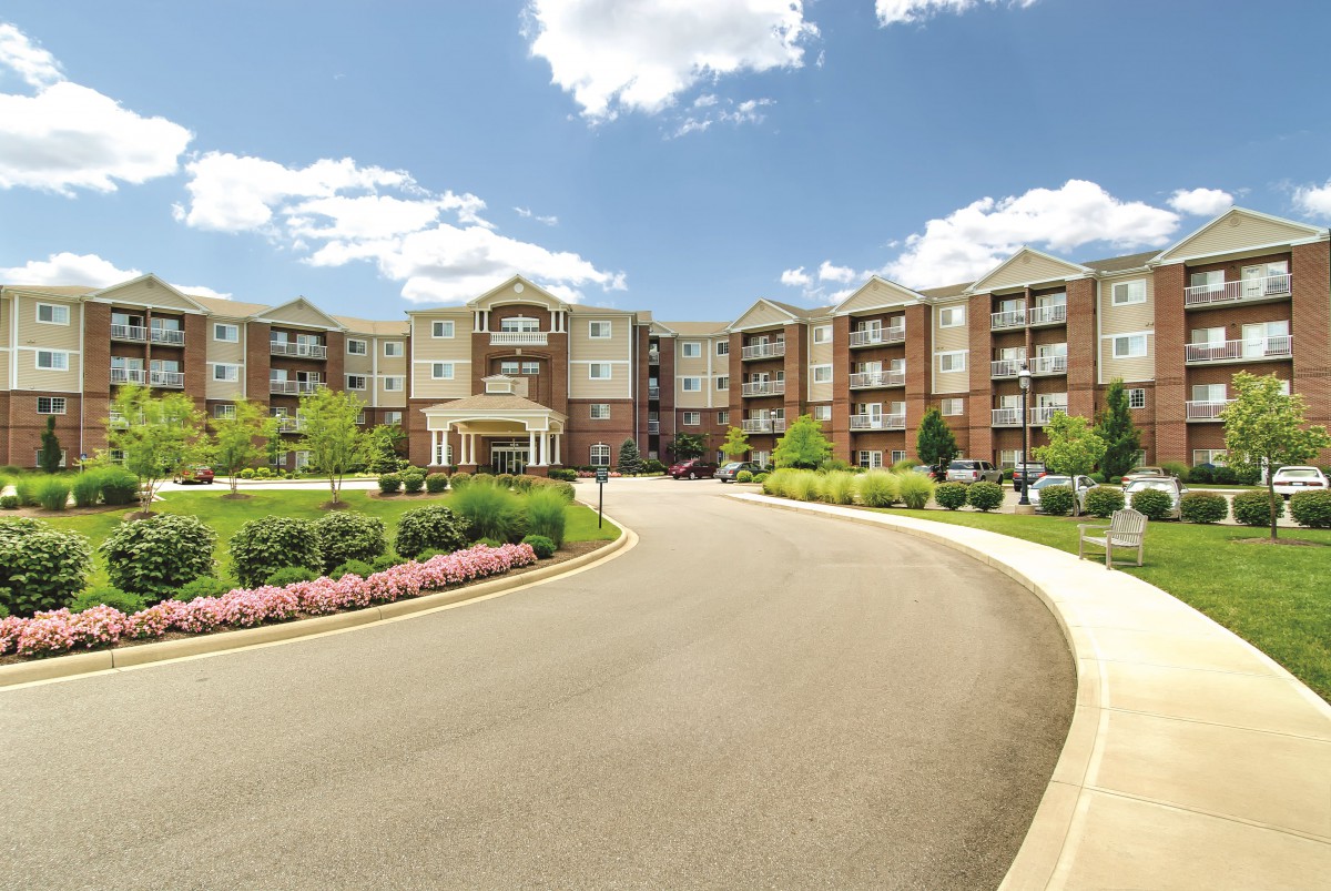 A modern residential apartment complex with a landscaped entrance and clear blue skies.